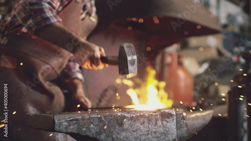 Close up of male blacksmith hammering metalwork on anvil with sparks and blazing forge in background - shot in slow motion photo