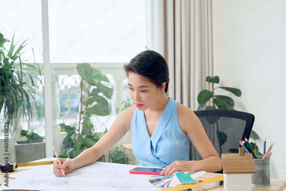 Asian female architect studying plans in office Asian female architect studying plans in office