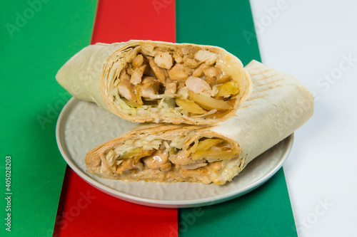 Close up Chicken shawarma roll with French fries, cucumber, cabbage served on gray plate, colorful red, white, green abstract background. Donner Street food rolled in thin lavash bread. Wrapped gyros
 photo