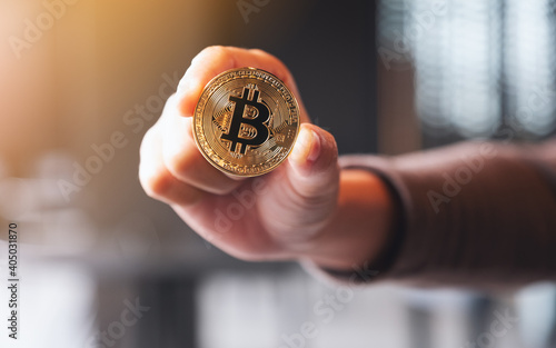 Closeup image of a hand holding and showing a golden color bitcoin