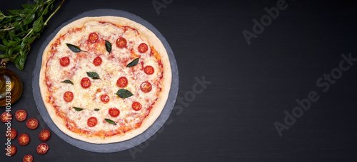 margherita pizza made with mozzarella cheese, tomatoes and olive oil on a stone plate with a black background with copy space for advertising. The pizza is accompanied by its main ingredients.