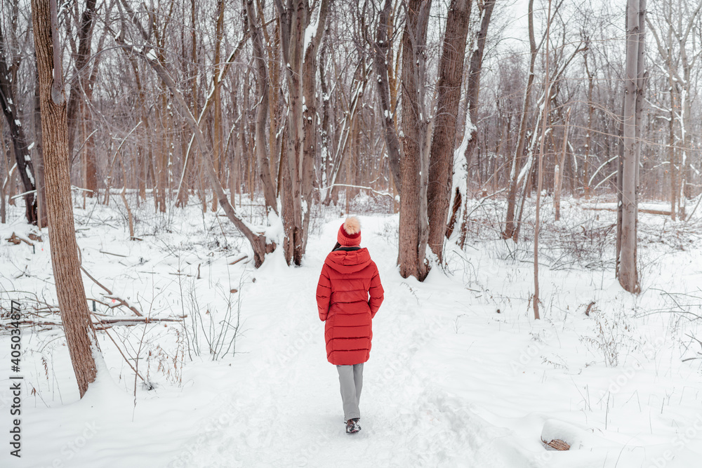 Winter nature walk woman walking in snowy forest trail outdoors. View from behind of woman in long red coat.