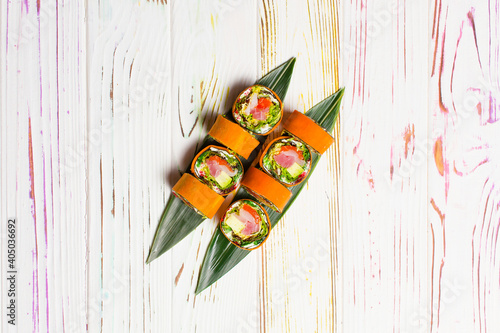 Directly above of Healthy Japanese rice free sushi roll served on bamboo leaves. Raw salmon, tuna, rockfish, avocado, lettuce, cream cheese wrapped in carrot daikon slices on light wooden background 