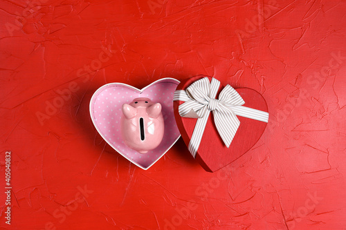 Fotografija Pink piggy bank in a heart shape gift box on red background.