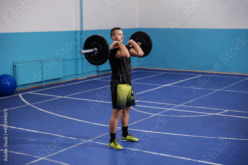 Fit muscular strong bodybuilder in sportswear lifting weights while standing in sport hall.