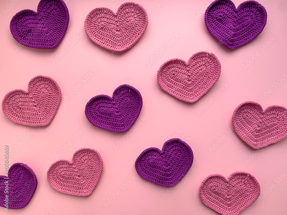 Crochet on the theme of Valentine's Day. In the photo, knitted pink and lilac hearts. Photo from above. The concept of creating a product. Knitted hearts on a pink background.