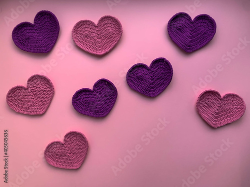 Crochet on the theme of Valentine s Day. In the photo  knitted pink and lilac hearts. Photo from above. The concept of creating a product. Knitted hearts on a pink background.