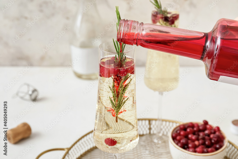 Pouring champagne into glasses with cranberry and rosemary on light table Pouring champagne into glasses with cranberry and rosemary on light table