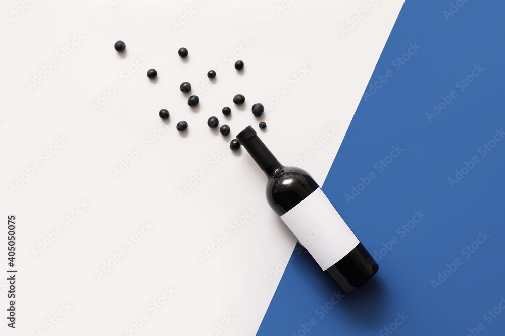 Fototapeta premium Bottle of wine with blank label and grapes on color background