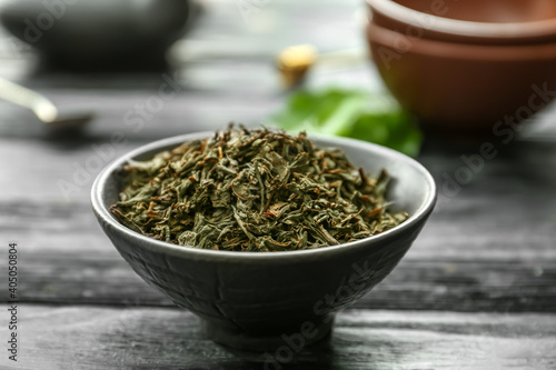 Dry black tea leaves in bowl on wooden background