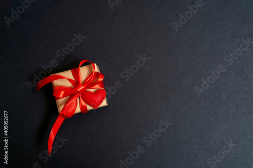 Top view of gift box wrapped in kraft paper with red ribbon on black background