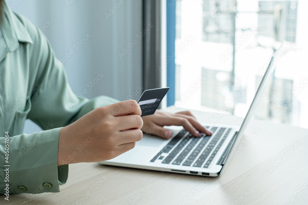 The businesswoman's hand is holding a credit card and using a laptop for online shopping and internet payment in the office The businesswoman's hand is holding a credit card and using a laptop for online shopping and internet payment in the office