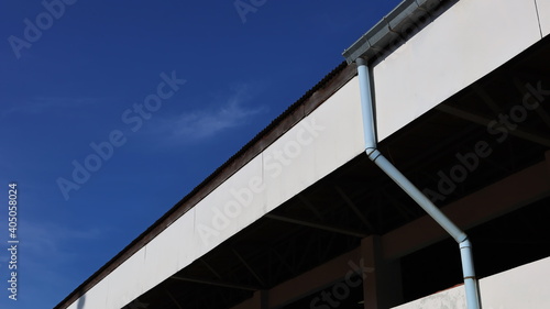 Gutter with drains below the roof. Galvanized rain gutter with plastic pipe below On building background and blue sky with copy space. Selective focus