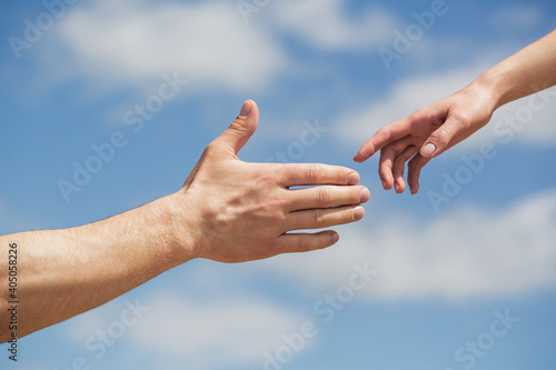 Giving a helping hand. Hands of man and woman on blue sky background. Lending a helping hand. Hands of man and woman reaching to each other, support. Solidarity, compassion, and charity, rescue © Yevhen
