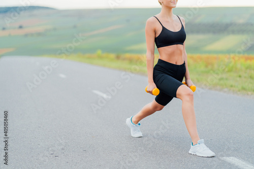 Athletic girl performs exercises with dumbbells, behind her road