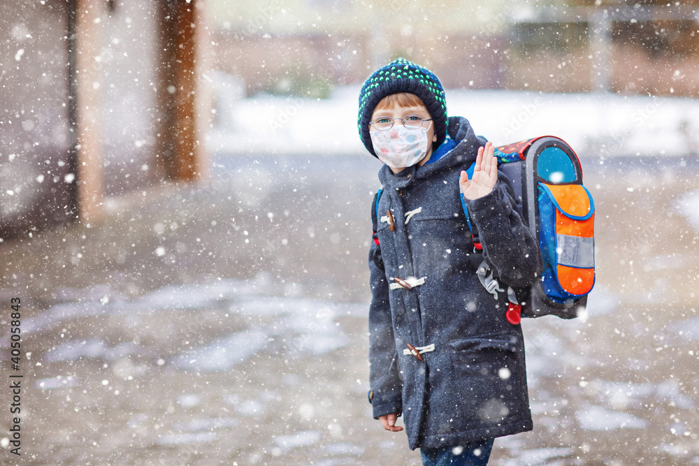 Fototapeta premium Little kid boy with glasses wearing medical mask on the way to school after lockdown. Child backpack satchel. Schoolkid on winter day with warm clothes. Quarantine time during corona pandemic disease