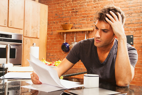 Caucasian man looking at paperwork in kitchen