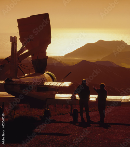 Two men standing beside aeroplane being filled with fertiliser at sunrise photo