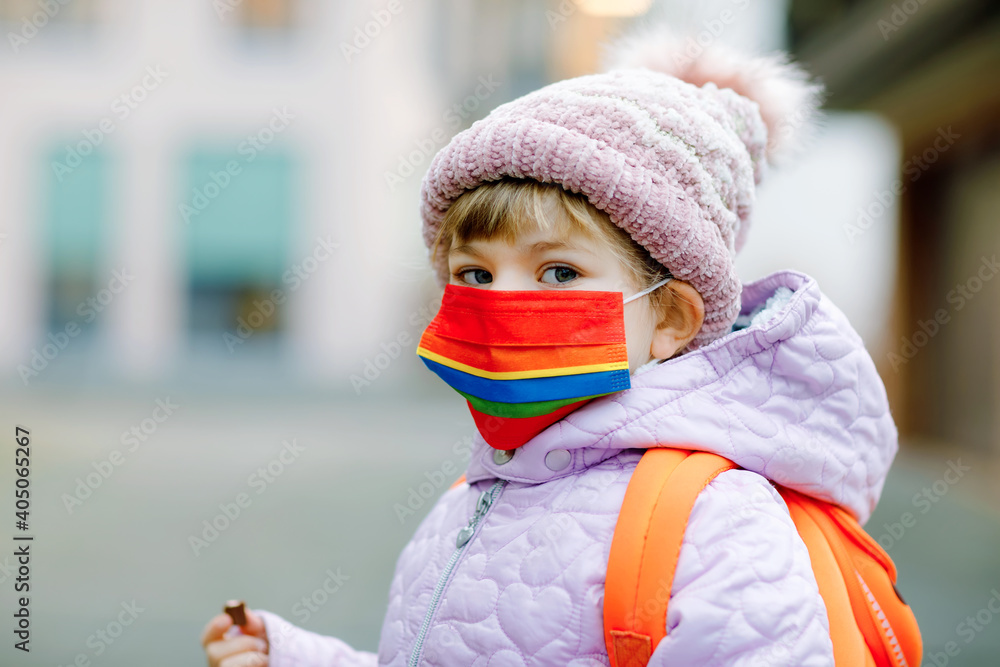 Little kid girl wearing medical mask on the way to kindergarten, playschool or nursery. Child with backpack satchel on cold day with warm clothes. Lockdown and quarantine time during corona pandemic - obrazy, fototapety, plakaty 
