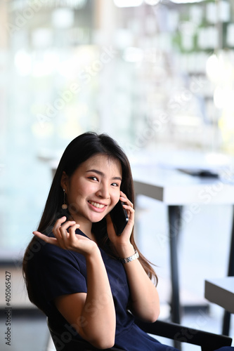 Free Download Portrait of happy businesswoman talking on mobile phone and smiling to camera while sitting in office. - GFXLoad