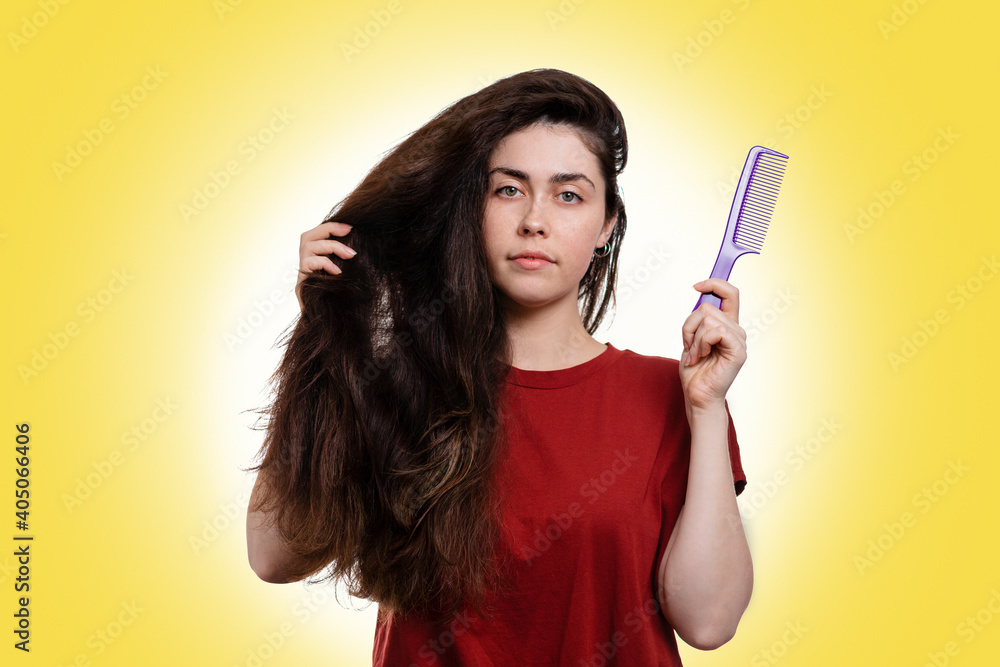 Portrait of a young caucasian woman holding her thick dark hair and comb for combing. White background. Hair care concept Portrait of a young caucasian woman holding her thick dark hair and comb for combing. White background. Hair care concept
