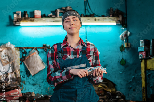 Portrait of a young smiling female mechanic in uniform, posing with gloves in her hands. Working room in the background. The concept of gender equality © _KUBE_