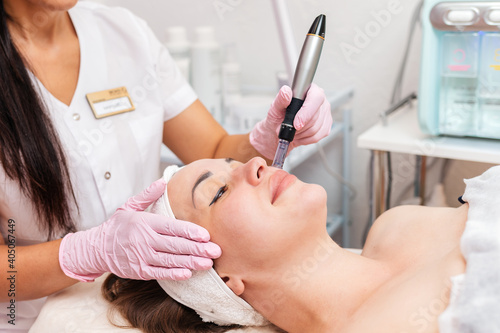 Beauty salon. Smiling cosmetologist in rubber gloves makes fractional mesotherapy of the face to the client. Close up of face. Concept of professional modern cosmetology and treatment