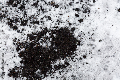 The texture of the ground in the snow. New background image of black earth on white snow