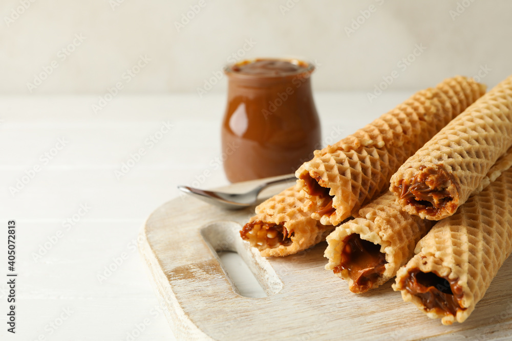 Board with wafer rolls with condensed milk on wooden background - obrazy, fototapety, plakaty 