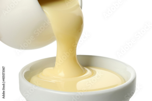 Condensed milk pouring in bowl, isolated on white background