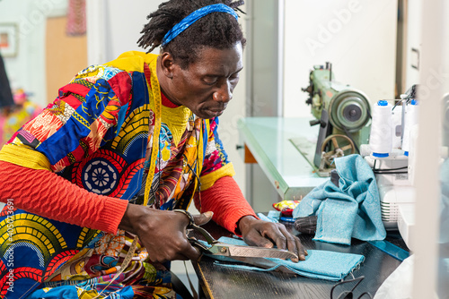 african tailor from senegal at work in his workshop, handcrafted production of european fashion clothes with african wax fabrics, concept of diversity and integration, new small socialbusiness photo