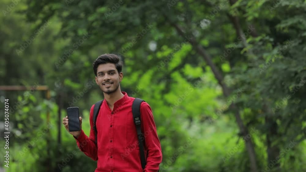 Young indian college student showing smart phone over nature background Young indian college student showing smart phone over nature background