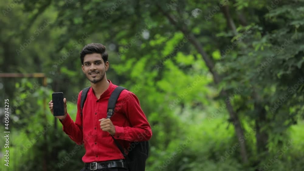 Young indian college student showing smart phone over nature background Young indian college student showing smart phone over nature background