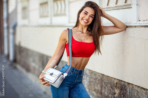 Outdoor portrait of young beautiful caucasuan woman with long straight hair holding leather handbag walking city street. photo