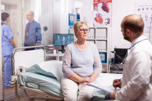 Elderly woman talking with doctor in hospital cabinet in the course of treatment. Elderly patient having a converstation with medical stuff in private clinic during consultation.