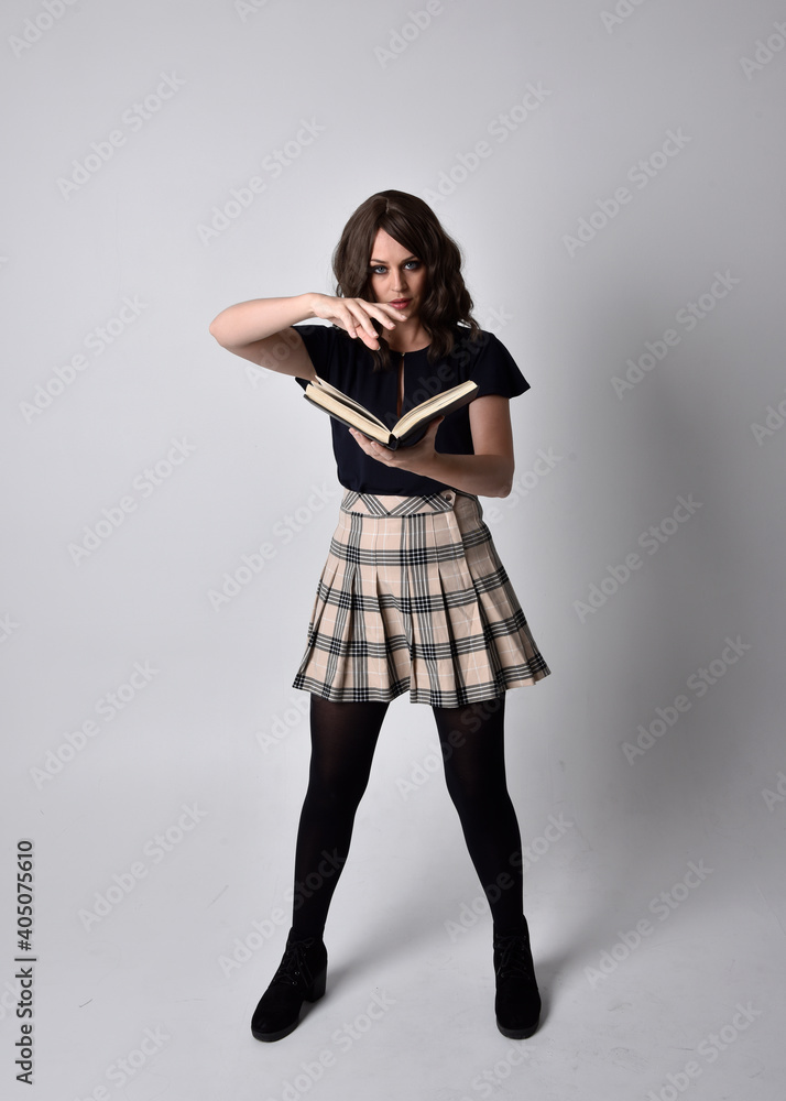 full length portrait of pretty brunette woman wearing tartan skirt and boots. Standing pose holding books against a studio background. full length portrait of pretty brunette woman wearing tartan skirt and boots. Standing pose holding books against a studio background.