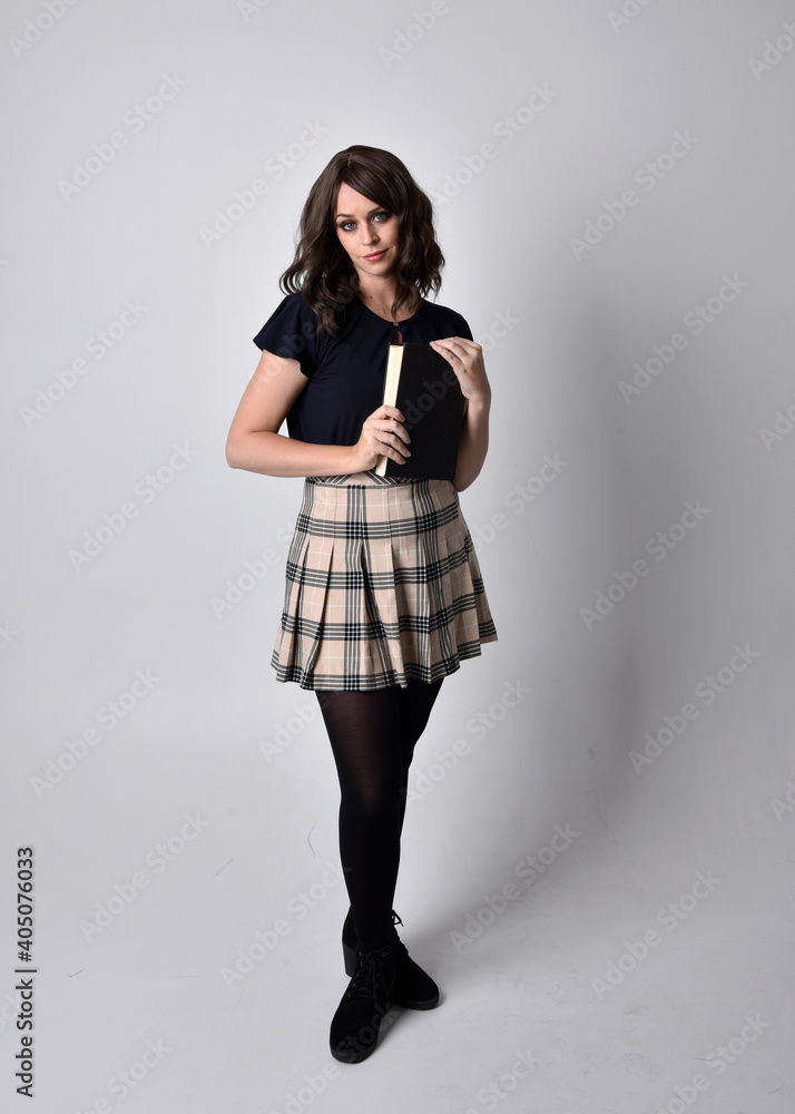 full length portrait of pretty brunette woman wearing tartan skirt and boots. Standing pose holding books against a studio background. full length portrait of pretty brunette woman wearing tartan skirt and boots. Standing pose holding books against a studio background.
