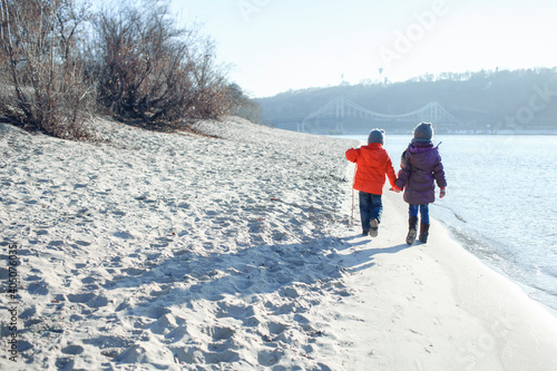 Family enjoying winter together, kids walking on the beach in winter, cold temperature and sunny day, love keep you warm, happy real people. Outdoors lifestyle