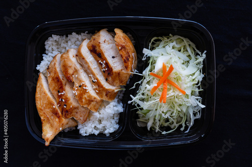 Grilled teriyaki chicken with rice in a lunch box on black background.