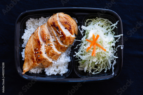 Grilled teriyaki chicken with rice in a lunch box on black background.