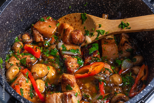 Cooking spicy pork stew with mushrooms in oriental style in a saucepan with spices, hot peppers and green onions - top view, close-up photo