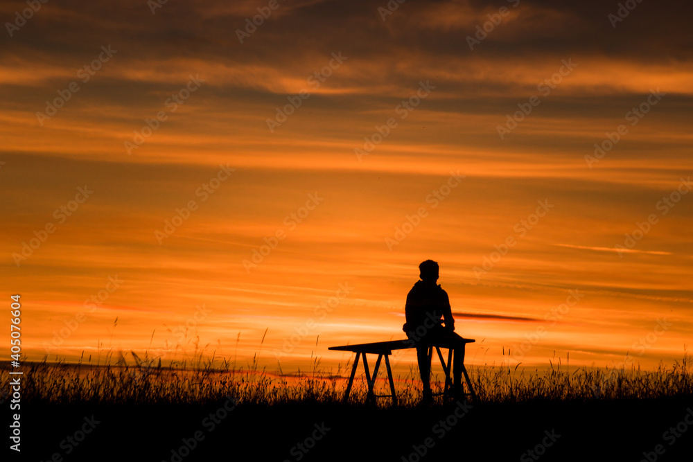 adolescent en train d'admirer un coucher de soleil en été, on ne voit que sa silhouette