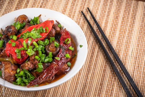 Bowl with spicy stewed pork with mushrooms in oriental style with spices, hot pepper on a bamboo napkin - top view, close-up photo