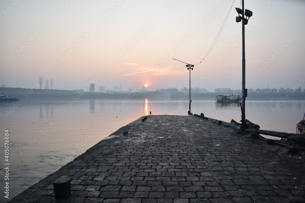 dock with sunrise view and reflection of sun on water with street lights and boat at essel world ,Gorai ,Mumbai