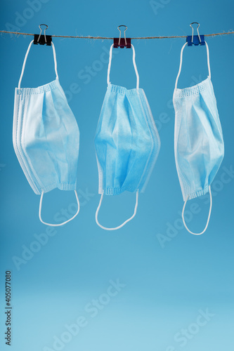 Three surgical masks hang on a clothesline against a blue background.