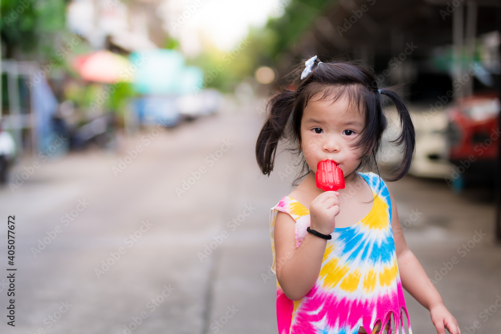Cute child eats a red jelly popsicle. In the summer, Happy children. Kid look at the camera. Toddler wear colorful clothes. baby 3-4 years old.