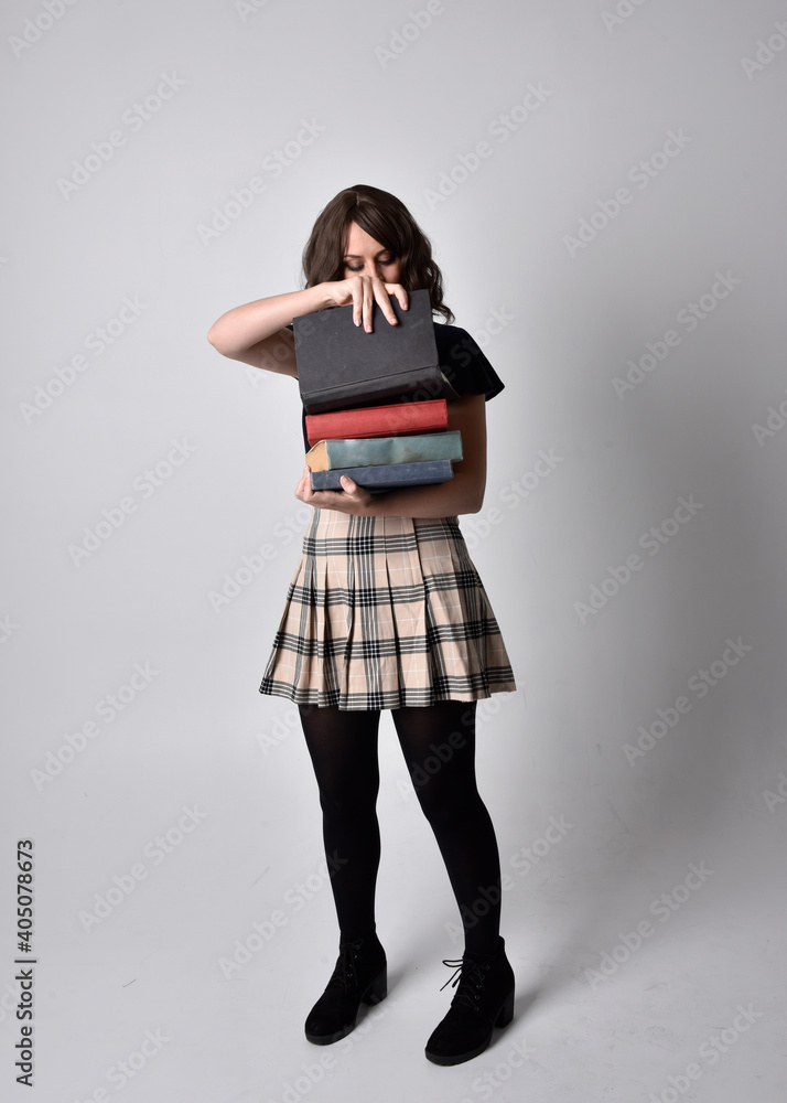 full length portrait of pretty brunette woman wearing tartan skirt and boots. Standing pose holding books against a studio background. full length portrait of pretty brunette woman wearing tartan skirt and boots. Standing pose holding books against a studio background.