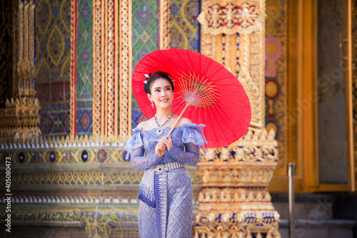 THAILAND, Beautiful woman in a pink Thai dress or a traditional Thai dress is spreading a red umbrella in a Thai temple. © NITIKAN T.