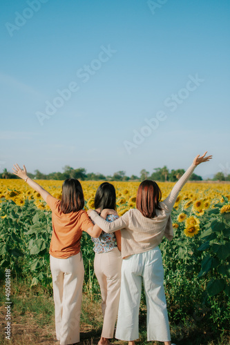 Three young women standing in the middle of yellow sunflowers field. Traveling together in countryside. Eco tourism concept.
