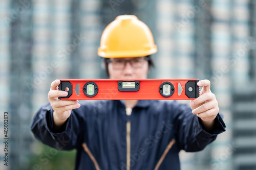 Asian maintenance worker man holding red aluminium spirit level tool or bubble levels at construction site. Equipment for civil engineering project